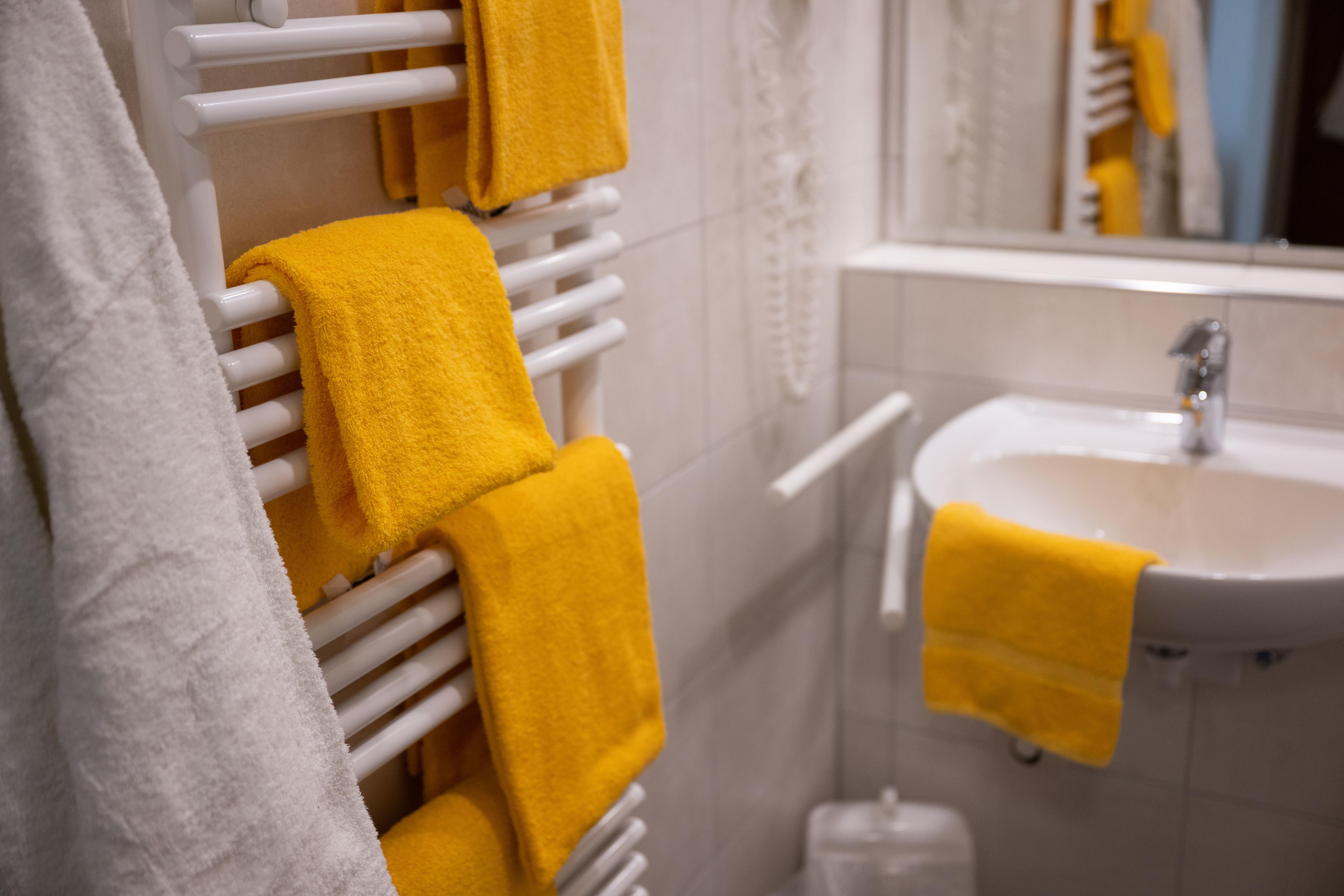 Blick ins Badezimmer: an einem weißen Heizkörper hängen drei gelbe Handtücher. Rechts ist das Waschbecken zu sehen, darüber hängt ein Spiegel. 