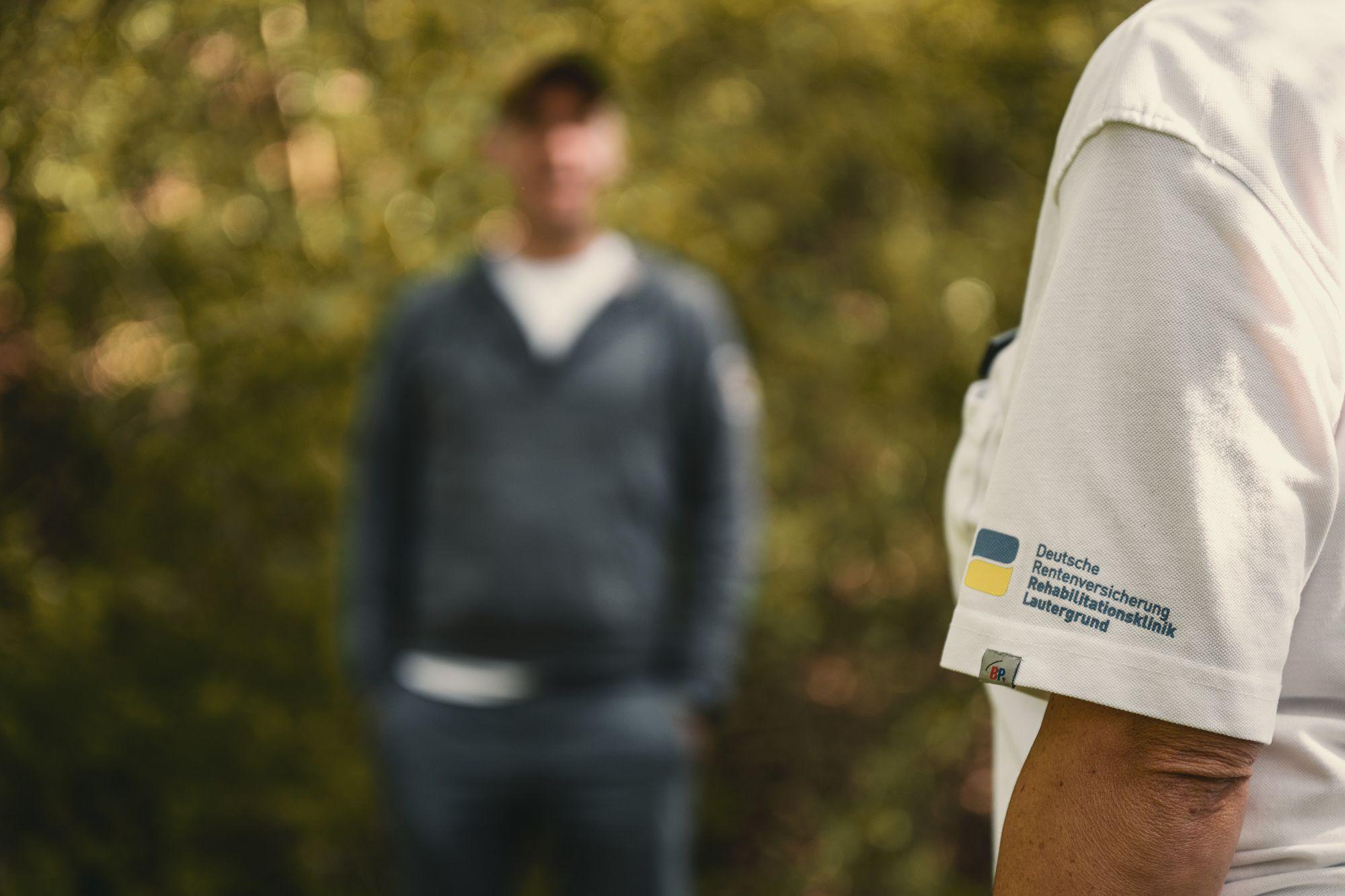 Ein Mann mittleren Alters unschaf bespricht im Freien Übungen mit einem Therapeuten im Vordergrund.