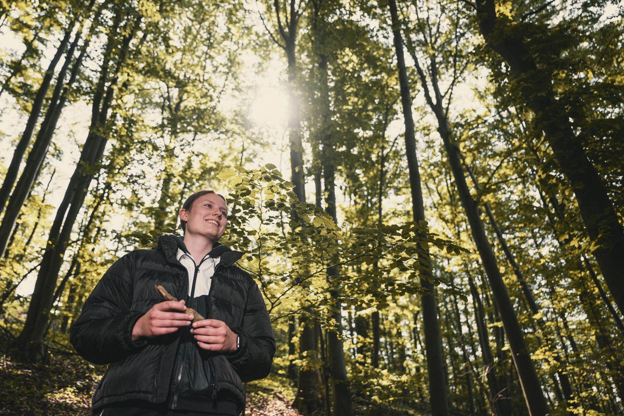 Eine Frau geht im Wald spazieren und die Sonne scheint durch die Bäume.