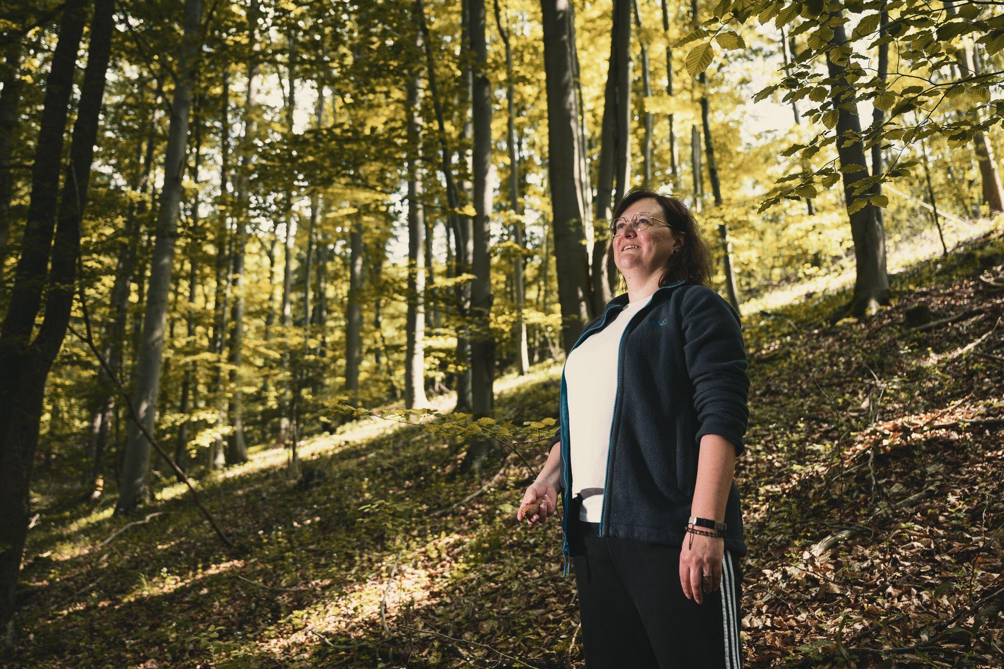 Eine Frau geht im Wald spazieren und die Sonne scheint durch die Bäume.