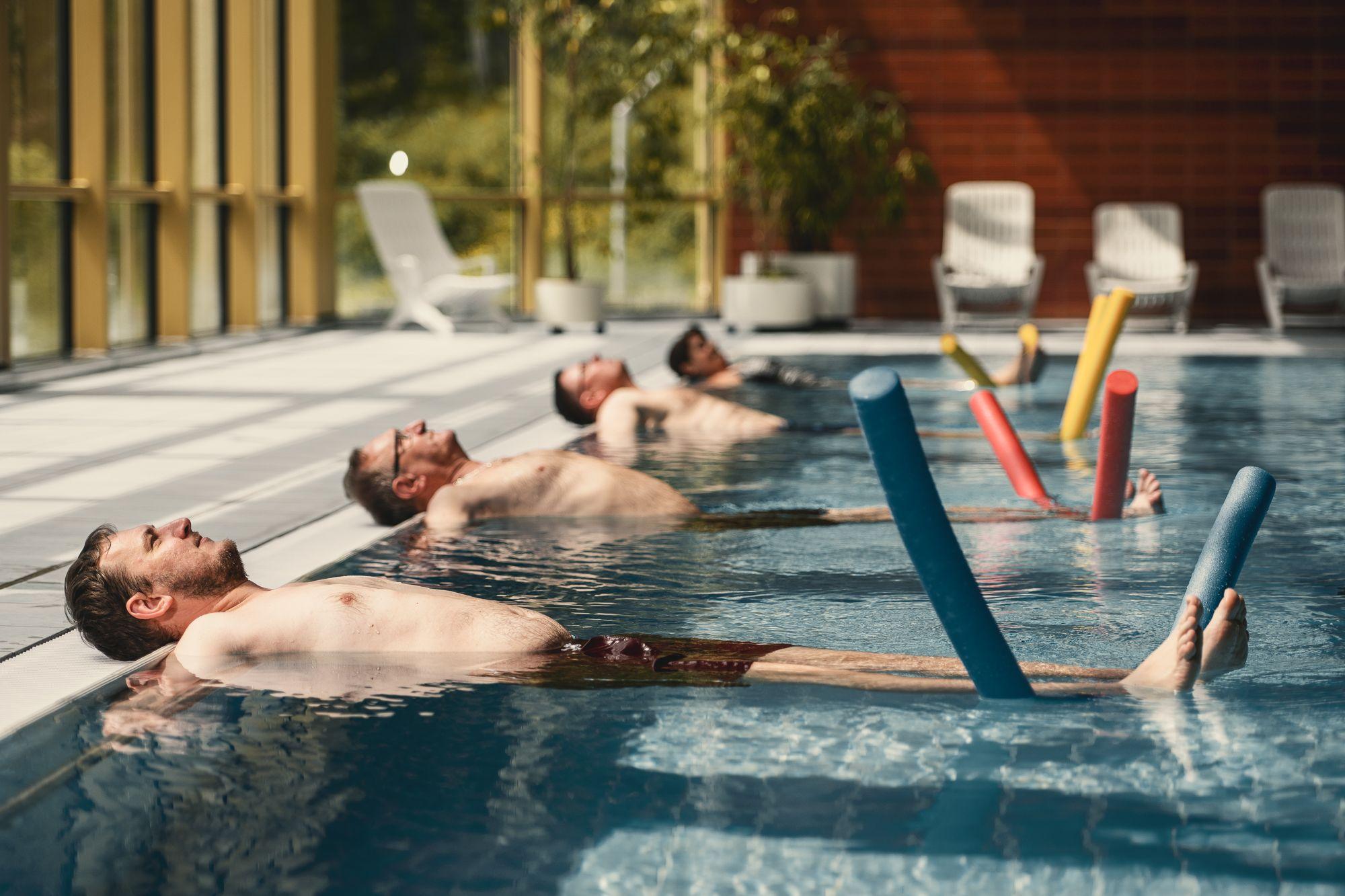 Im Schwimmbad machen mehrere Patienten Übungen mit einer Schwimmnudel.