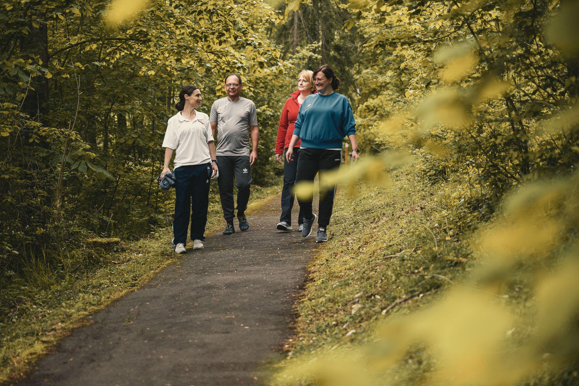 Eine Gruppe Patienten geht auf einem Waldweg entlang. 