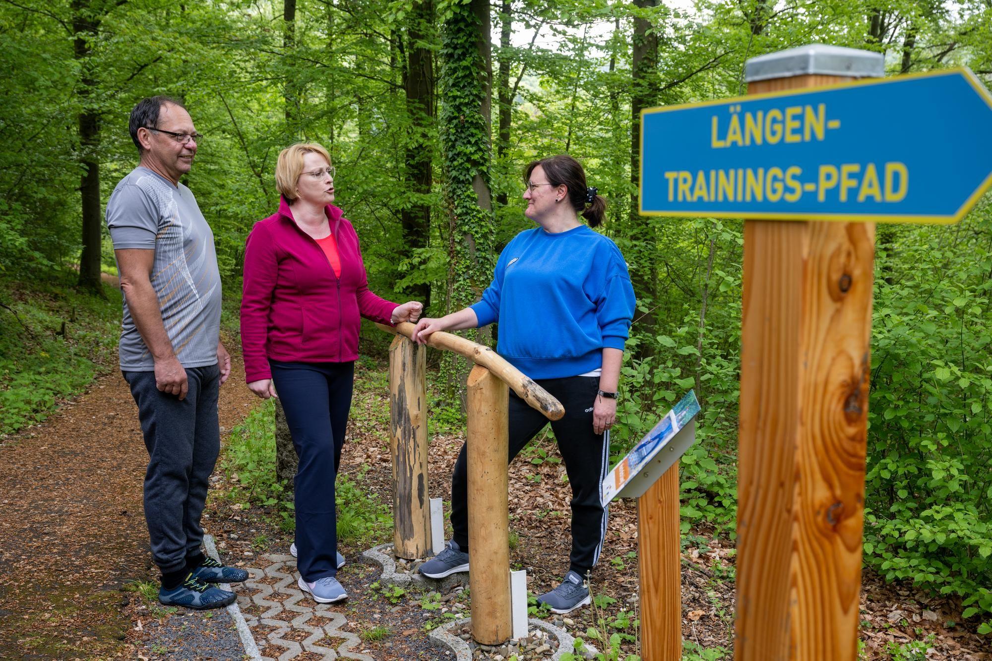 Ein Patient und eine Patientin mit einer Trainerin beim Längen-Trainings-Pfad im Wald.