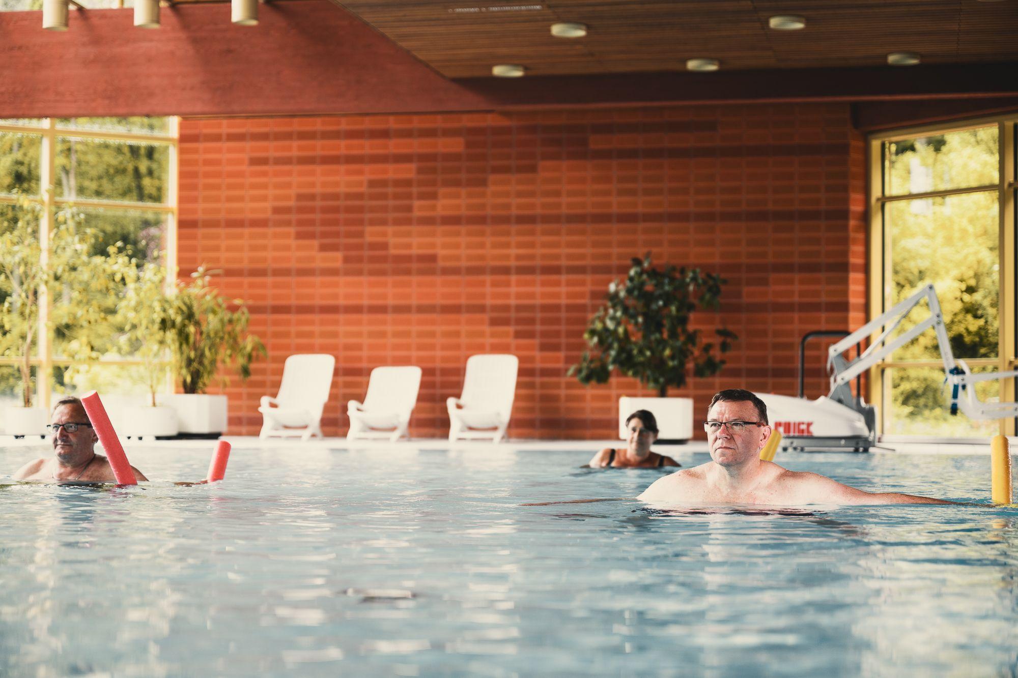 Im Schwimmbad machen mehrere Patienten Übungen mit einer Schwimmnudel.