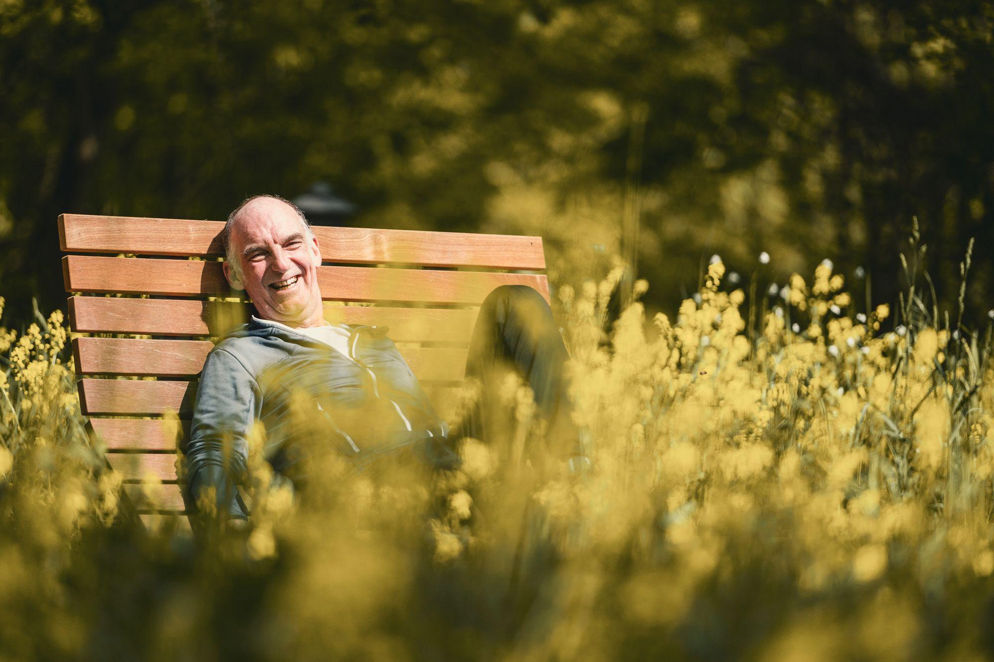 Ein älterer Mann sitz lächelnd auf einer Bank