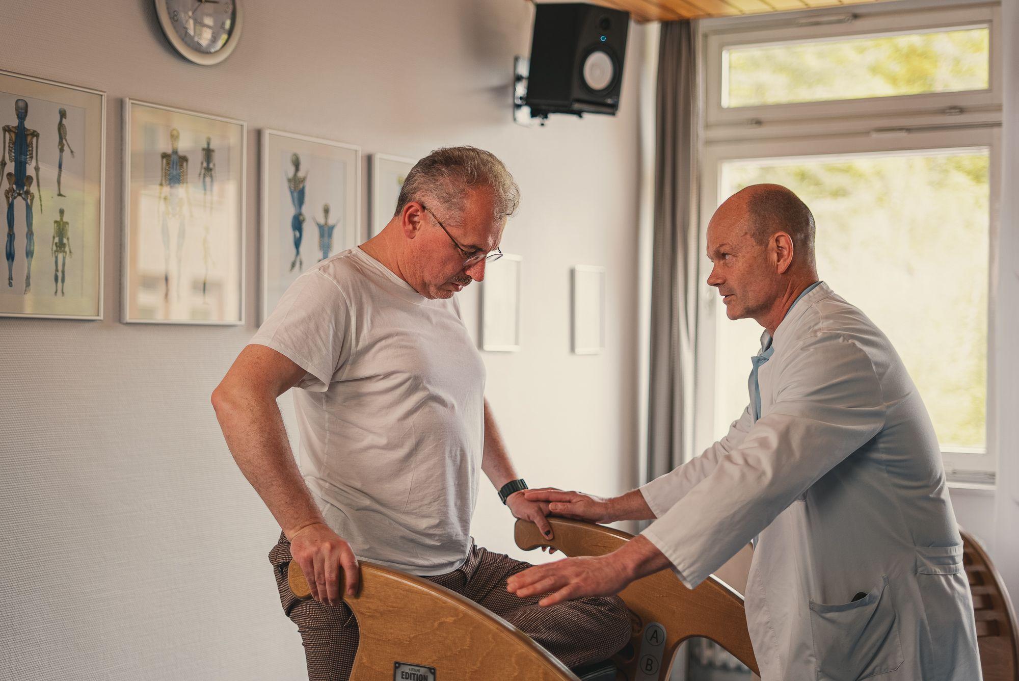 Mann mittleren Alters führt Gymnastikübungen unter der Aufsicht des Chefarztes durch.
