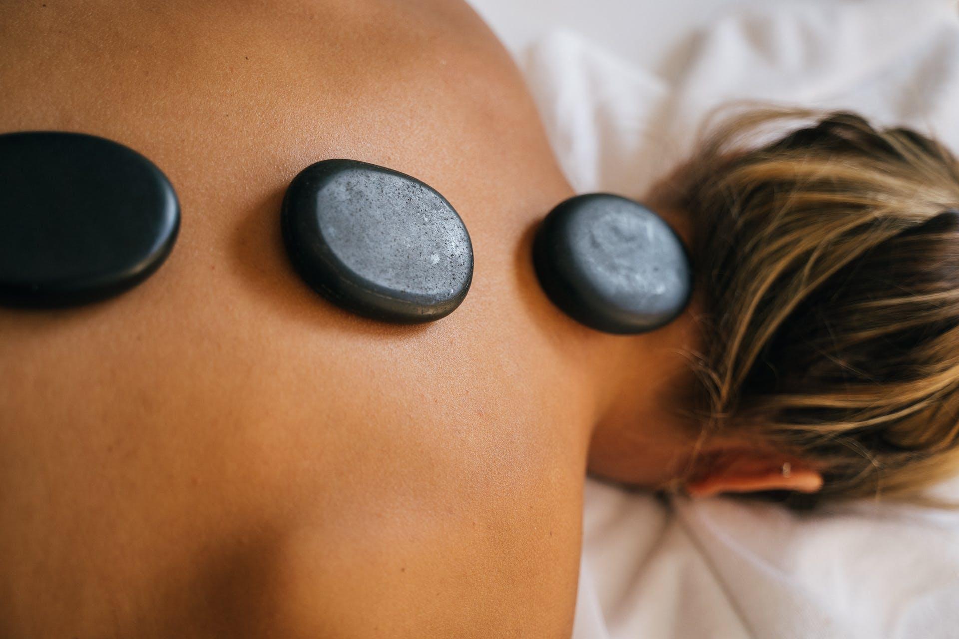 Hot Stone Massage, die Frau liegt auf dem Bauch und man sieht drei Steine auf Ihrem Rücken liegen.